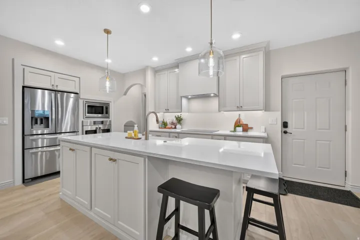 Central kitchen island with white countertop, recessed lighting, shaker-style cabinetry, stainless steel appliances, and wood-finish flooring