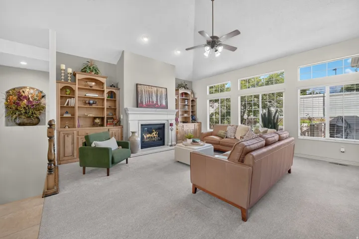 Vaulted ceiling with an attached ceiling fan, large windows with upper transoms, built-in shelving, and a fireplace with a mantel
