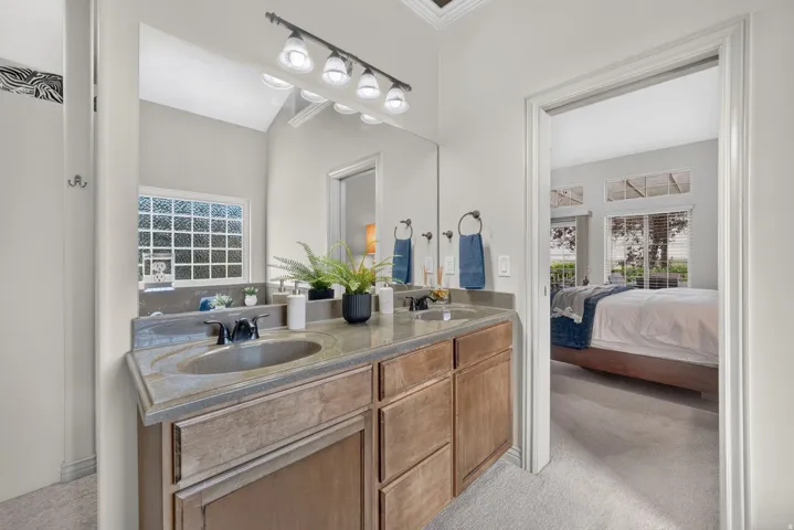 Dual vanity featuring integrated sinks, a wide mirror, a four-light fixture, and a glass block window