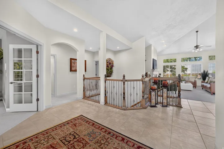 Vaulted ceiling with a ceiling fan, recessed lighting, tile flooring, wood and wrought iron staircase railing, and French doors