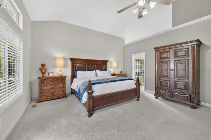 Vaulted ceiling, light neutral wall color, carpeted flooring, large window with blinds, ceiling fan with integrated lighting