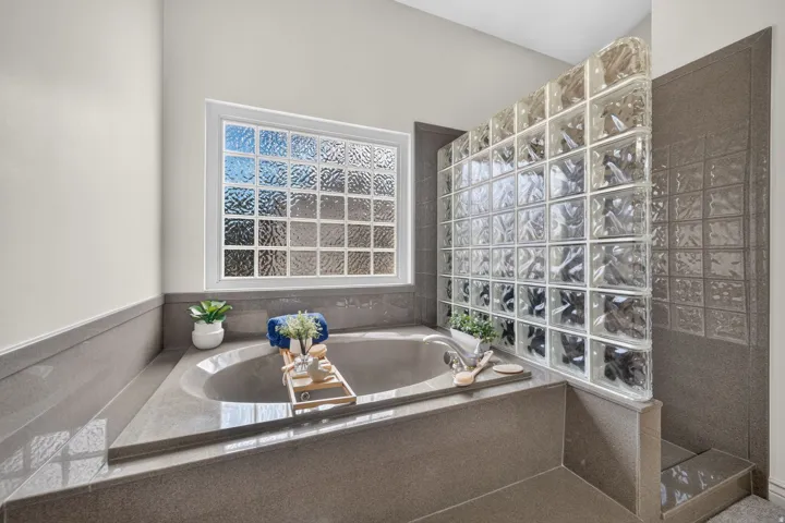 Built-in soaking tub with a tiled surround, privacy glass block wall, and a large window with obscure glass