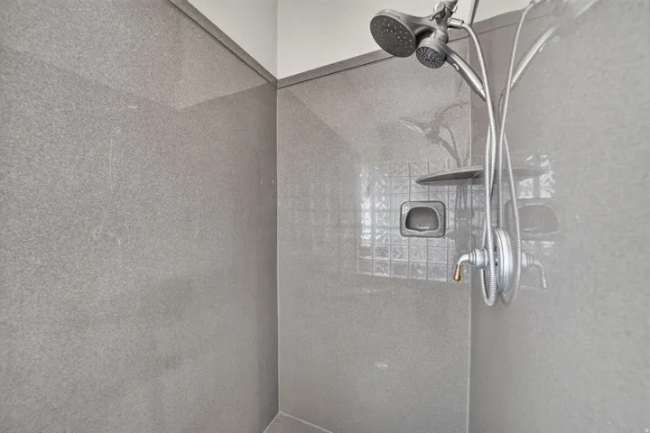 Shower enclosure with textured gray wall panels, a dual-head shower system, and an integrated soap dish