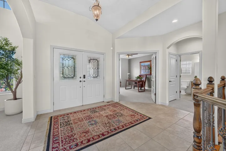 Entryway featuring dual paneled doors with decorative glass inserts, vaulted ceilings, and tile flooring
