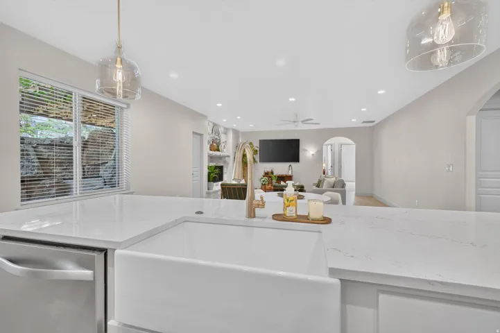 White countertop island with integrated farmhouse sink, stainless steel dishwasher, and clear glass pendant lighting