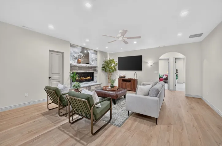 Recessed lighting, wood-finish flooring, stone-clad fireplace, ceiling fan, and arched doorway