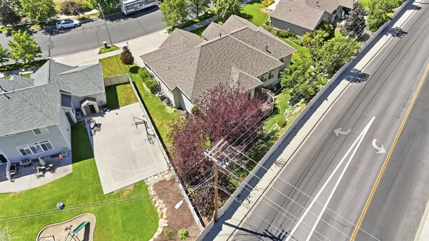 Spacious backyard with a concrete sports court, lush green lawn, mature landscaping, and a playground structure