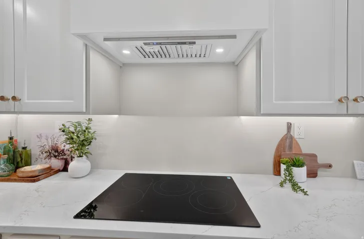Integrated cooktop with overhead range hood, light-toned cabinetry, and solid surface countertops