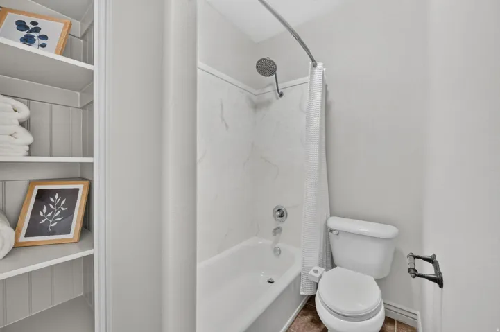 Tub and shower combination with a curved shower rod, wall-mounted shower head, and an adjacent toilet