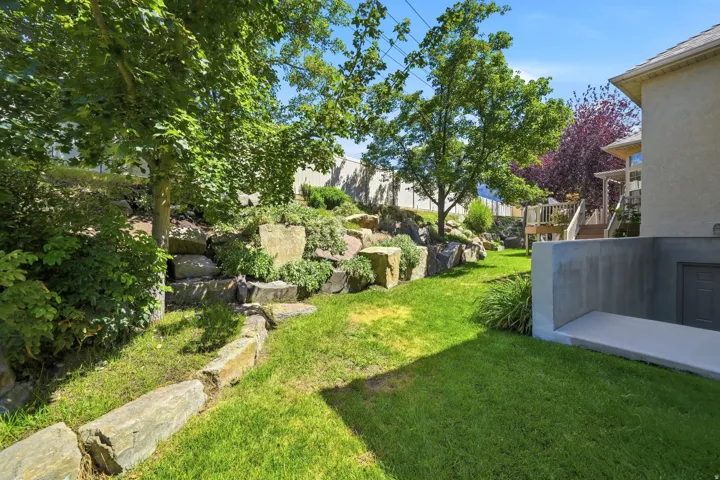 Expansive lawn with natural rock landscaping, mature trees, and a concrete patio