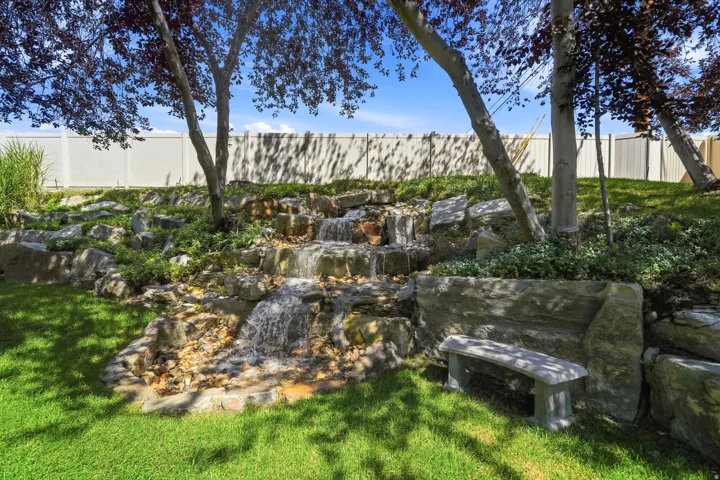 Expansive landscaped yard featuring a multi-tiered rock waterfall, a stone bench, and mature trees
