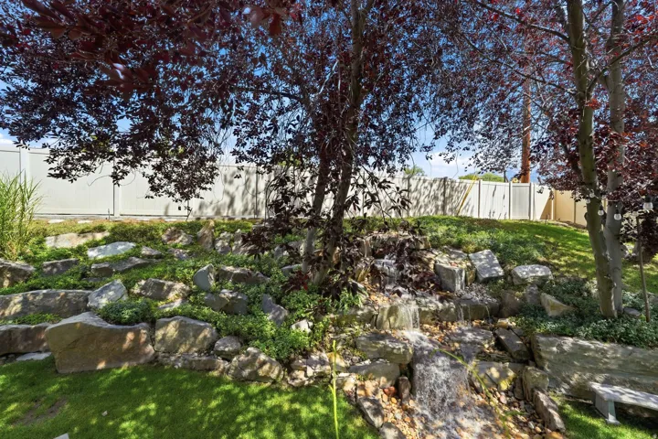 Landscaped yard featuring a rock waterfall, mature trees, and a privacy fence