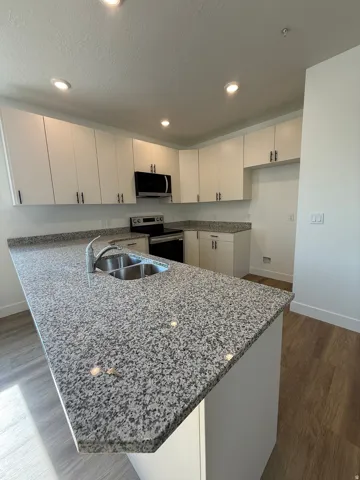 Kitchen featuring white cabinetry, granite countertops, stainless steel appliances, and wood-finish flooring