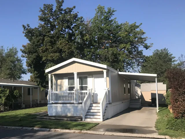 Front porch with white railings and columns, covered carport, manicured lawn, paved driveway