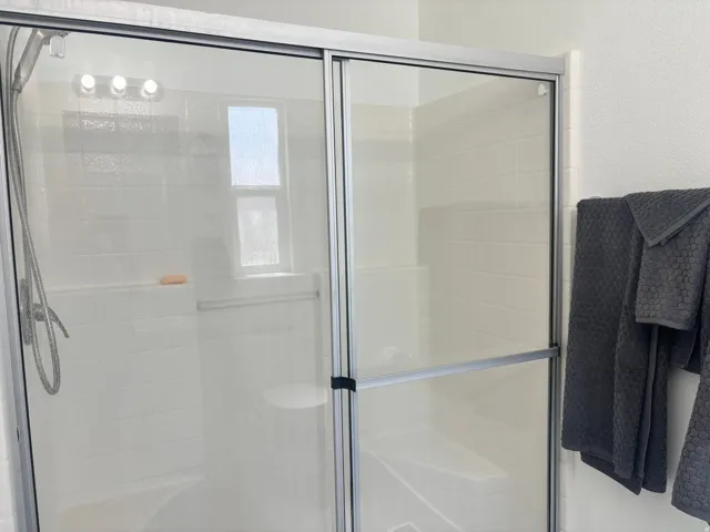 Walk in shower Sliding glass shower enclosure with white subway tile surround, built-in shower bench, and a built-in shower niche