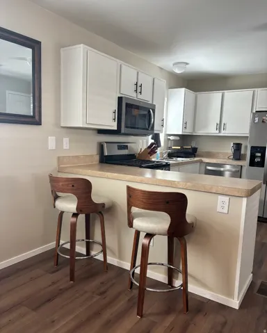 Kitchen featuring white cabinetry, light-colored countertops, stainless steel appliances, and wood-finish flooring