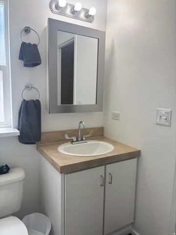 Vanity with a recessed sink, chrome faucet, wall-mounted mirror, and cabinet storage