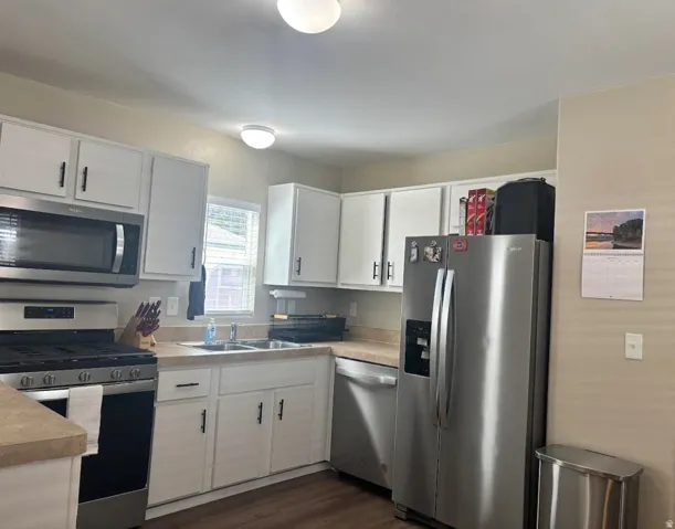 White cabinetry with matte black hardware, stainless steel appliances, wood-finish flooring, and a double-basin sink
