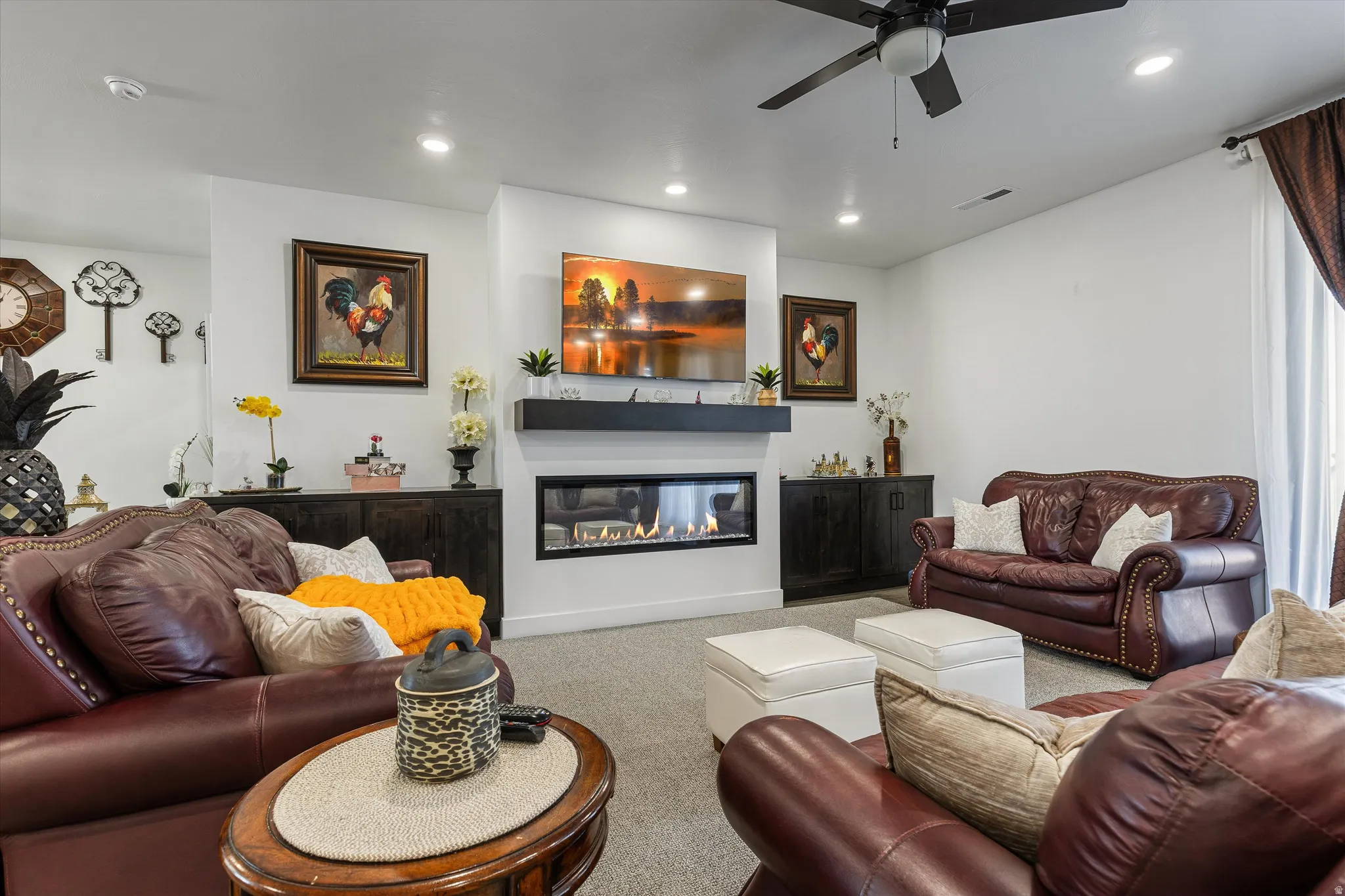 Recessed lighting, ceiling fan, built-in electric fireplace, wall-mounted floating shelf, and neutral carpeting