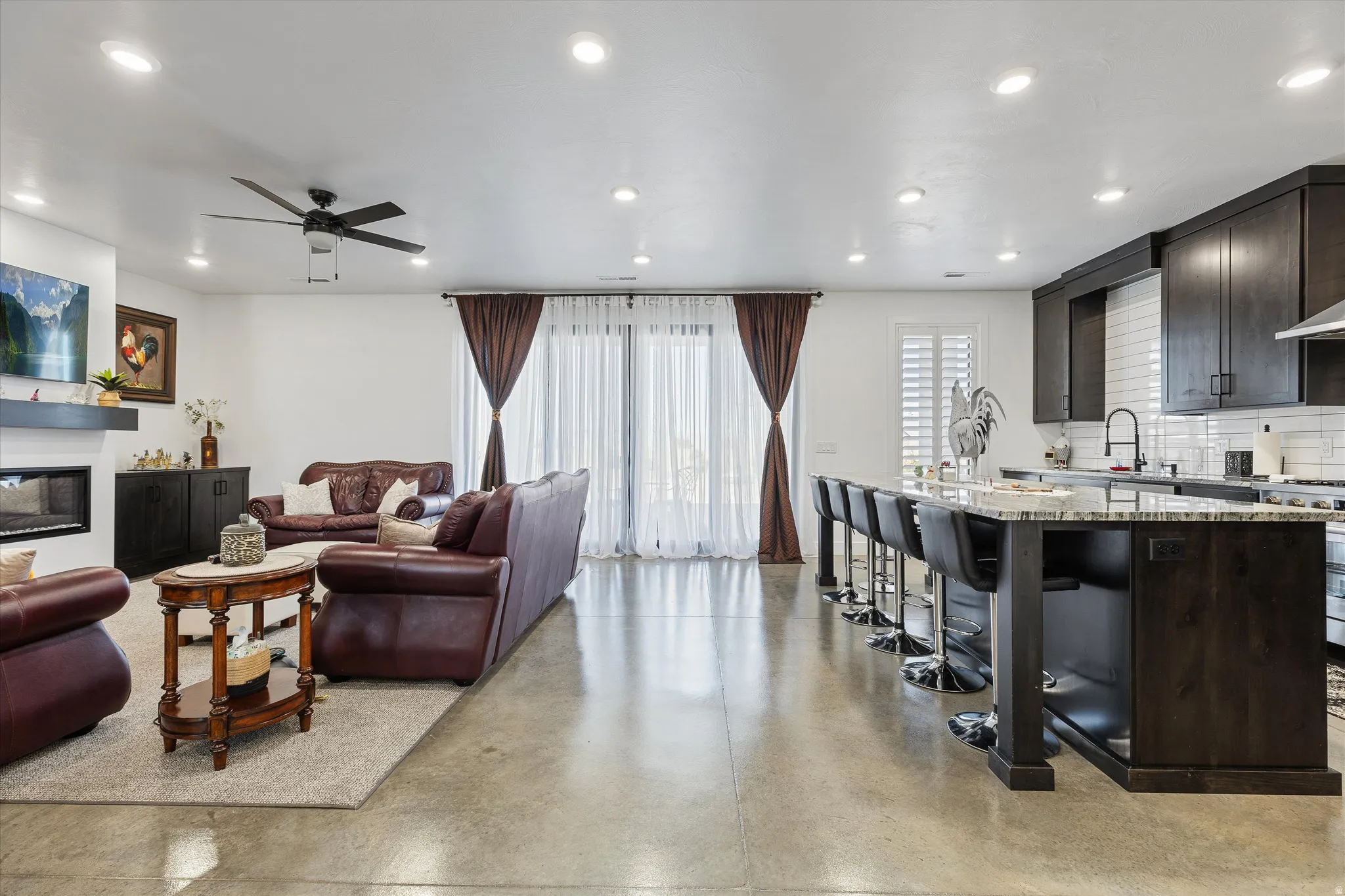 Open-concept living space featuring polished concrete flooring, a fireplace with a mantel, recessed lighting, and a kitchen island with seating