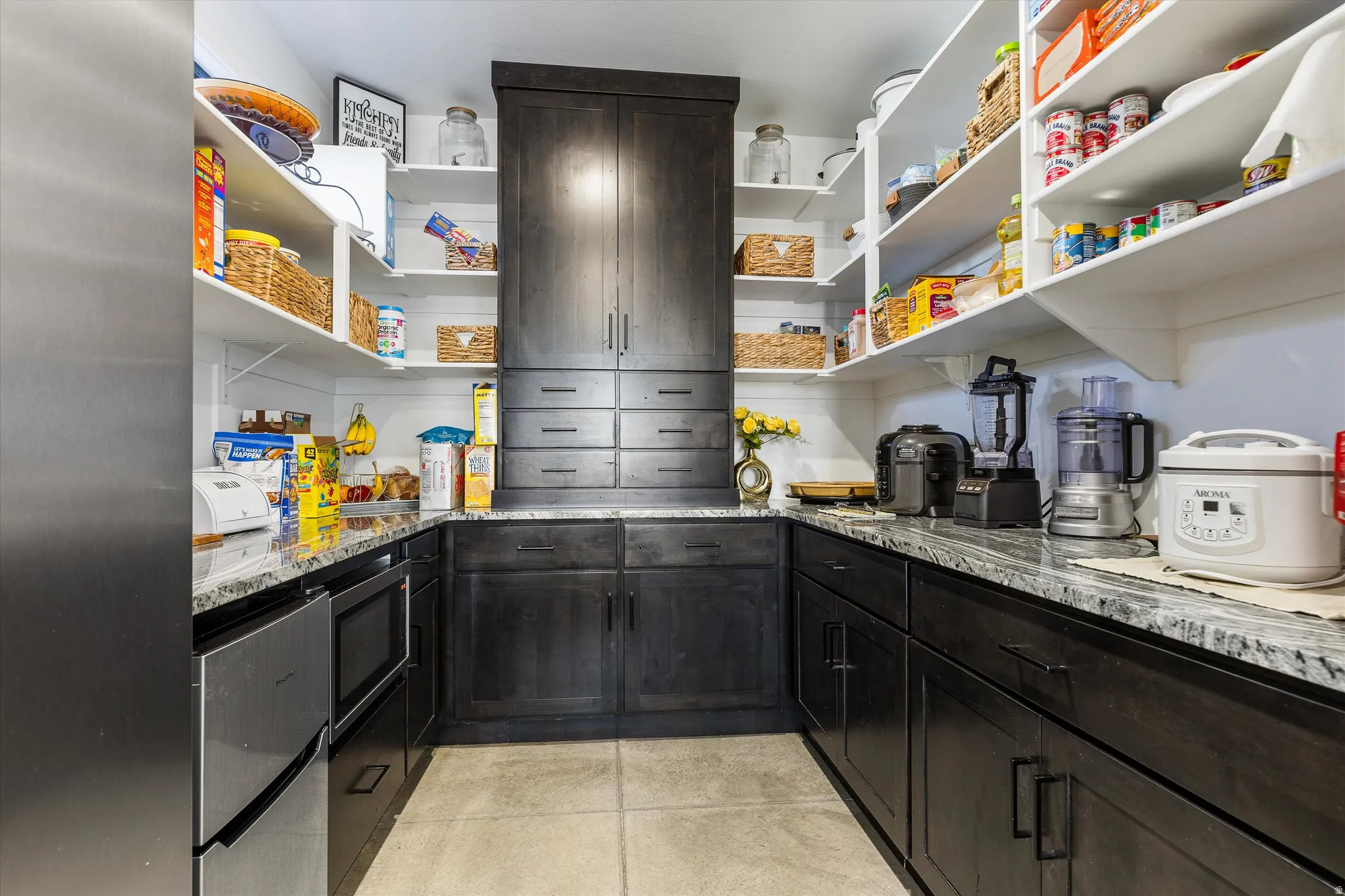 Spacious butler's pantry featuring dark wood-finish cabinetry, extensive white shelving, integrated stainless steel appliances, and durable light-toned flooring