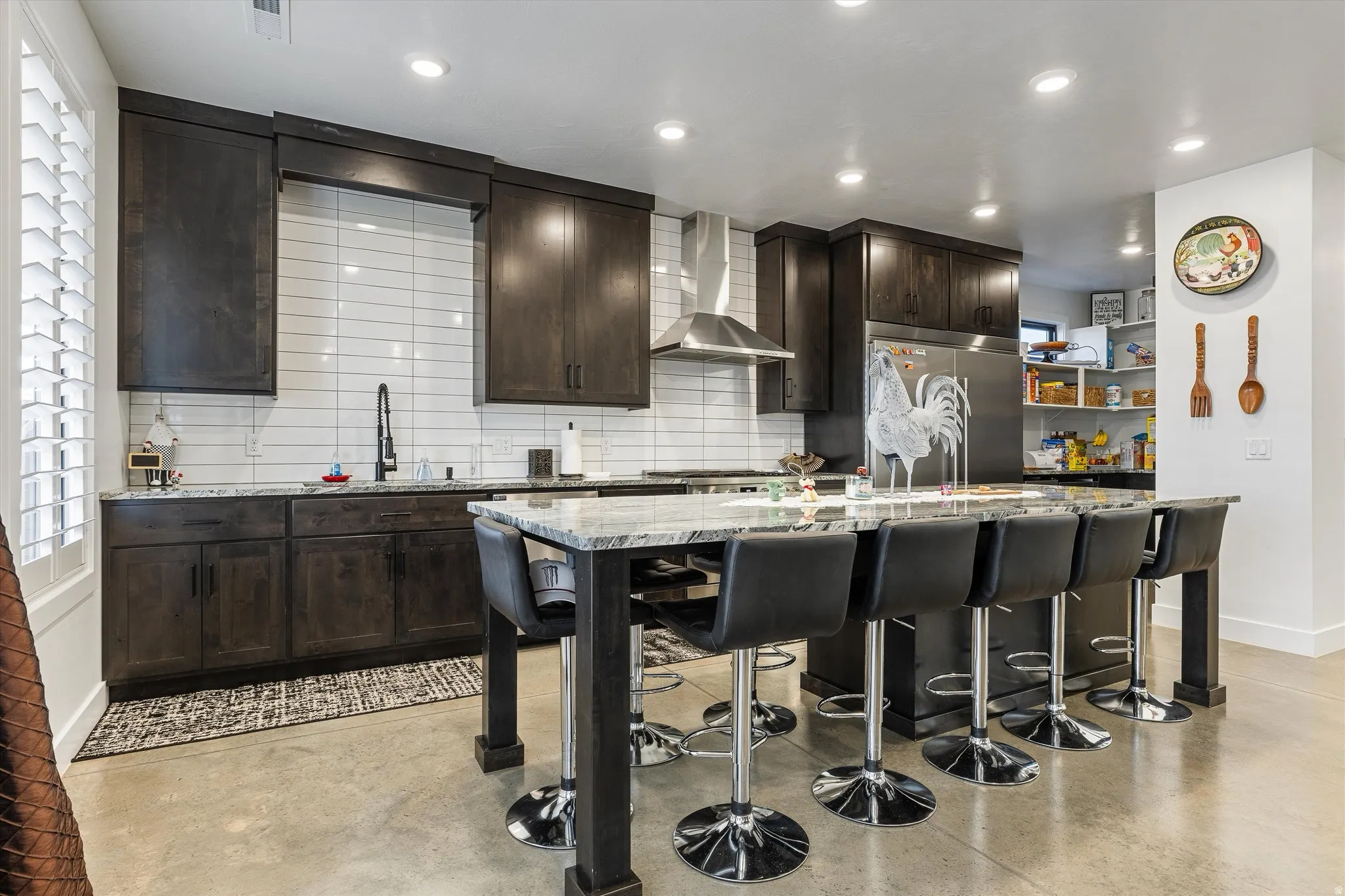 Kitchen featuring dark wood-finish cabinetry, stainless steel appliances, a tile backsplash, an island with a light-toned countertop, and recessed lighting