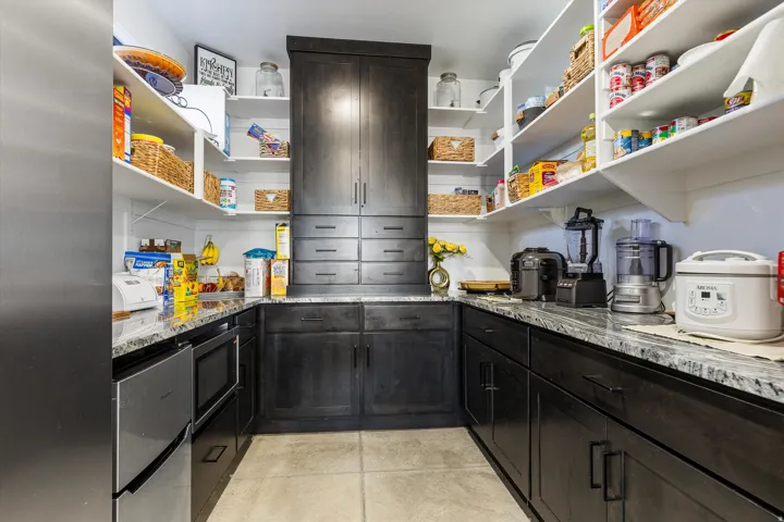 Spacious butler's pantry featuring dark wood-finish cabinetry, extensive white shelving, integrated stainless steel appliances, and durable light-toned flooring