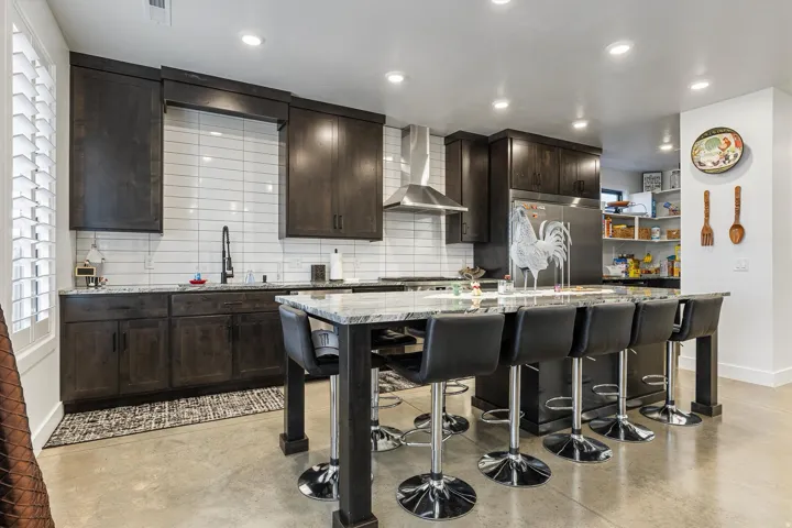 Kitchen featuring dark wood-finish cabinetry, stainless steel appliances, a tile backsplash, an island with a light-toned countertop, and recessed lighting