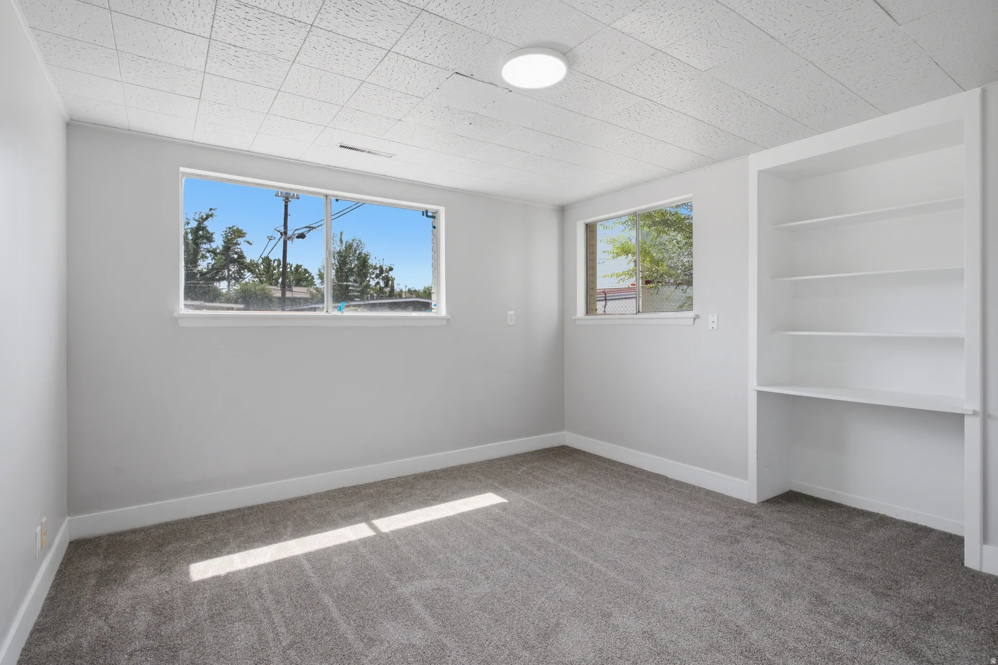 Built-in shelving, flush-mount ceiling light, two windows, and textured ceiling