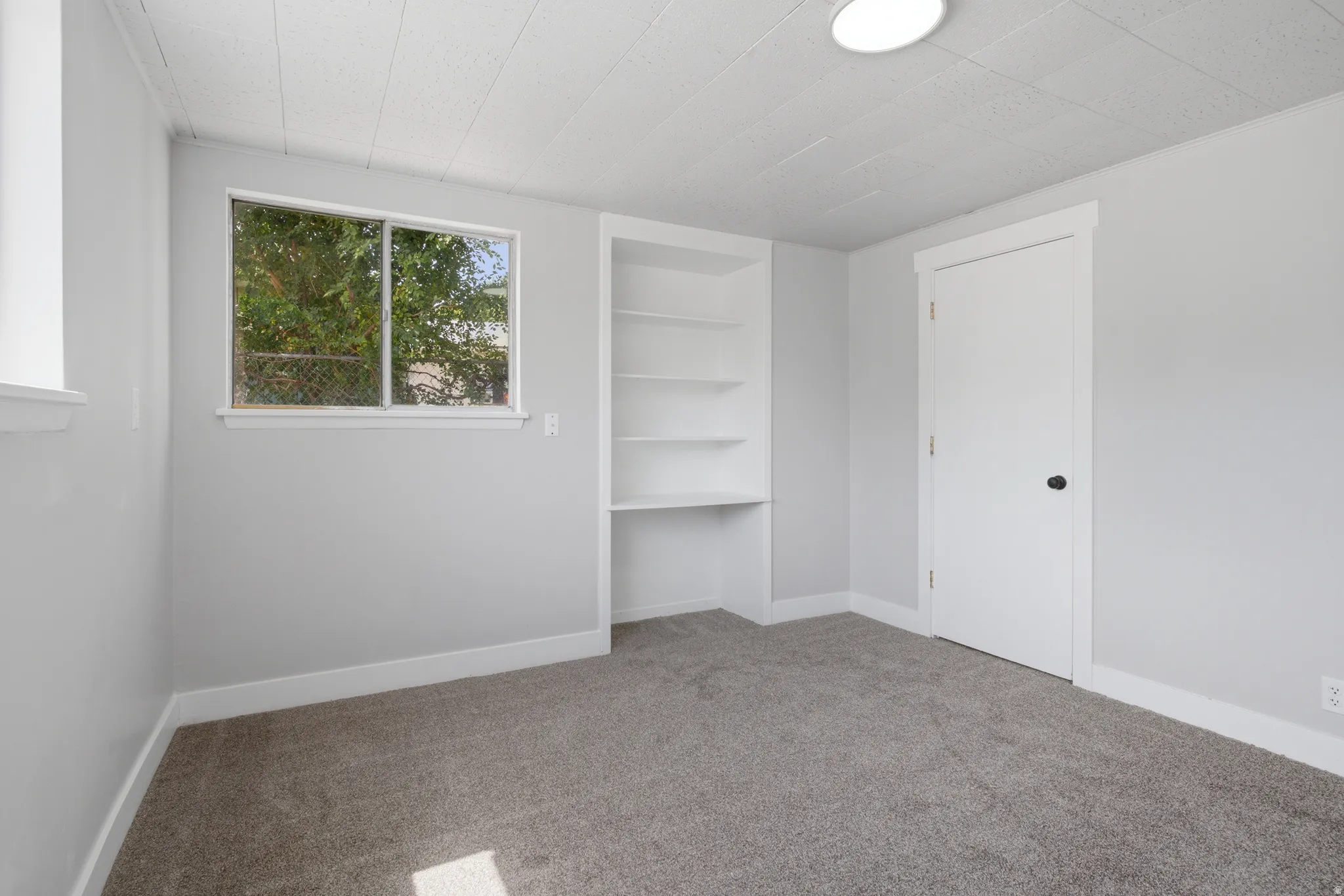 Built-in shelving with desk space, light gray walls, dark gray carpet, white trim, and a flush mount ceiling light