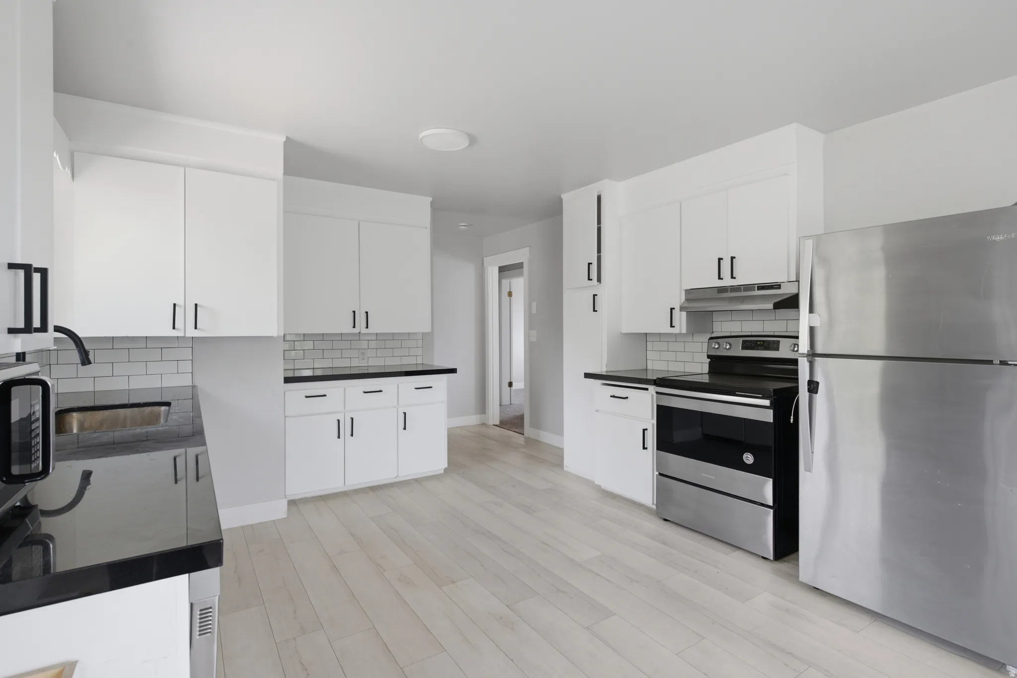 Modern kitchen featuring white cabinetry, dark countertops, a subway tile backsplash, stainless steel appliances, and light wood-finish flooring