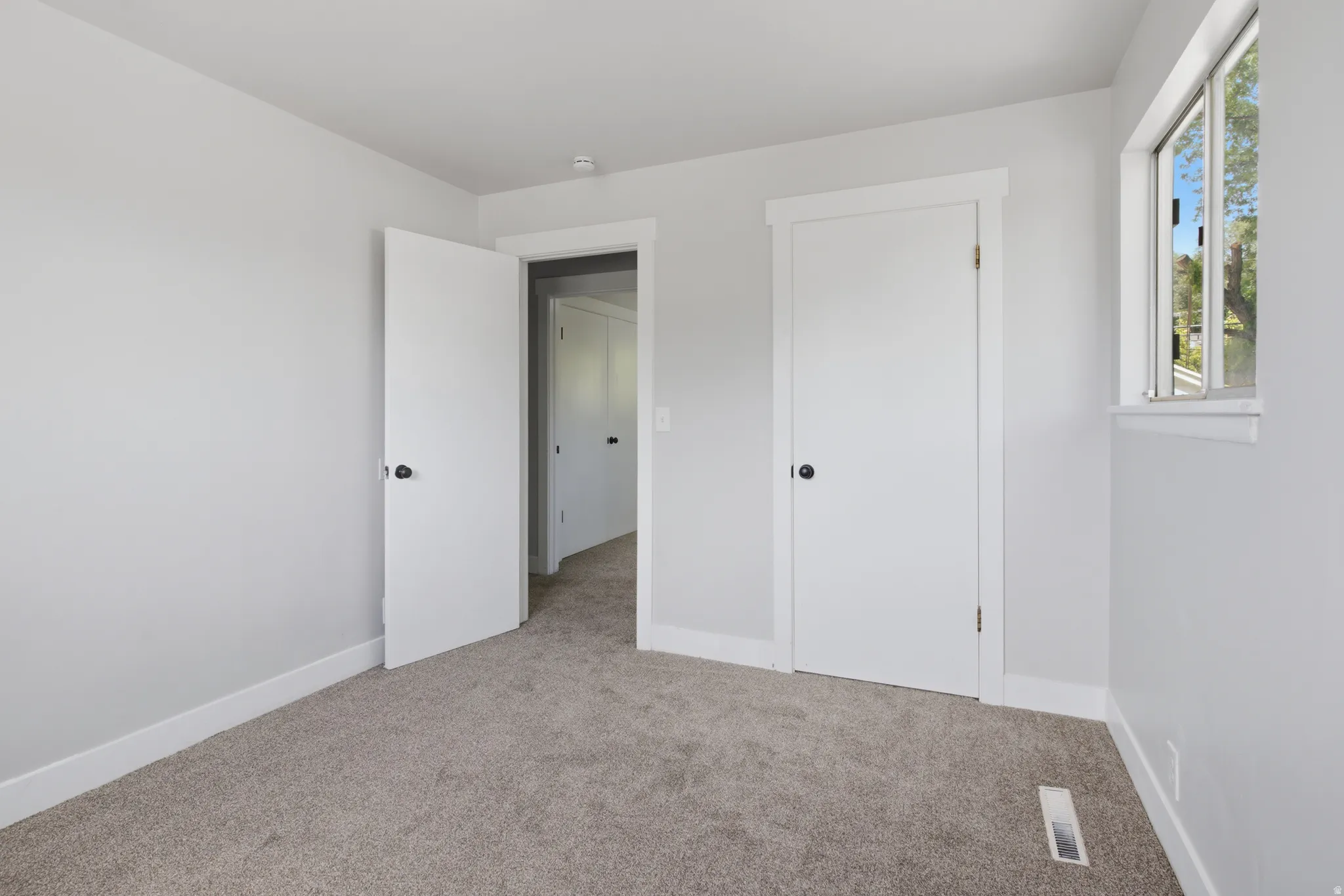 Grey carpeting, white trim, white doors, and a window with a white frame