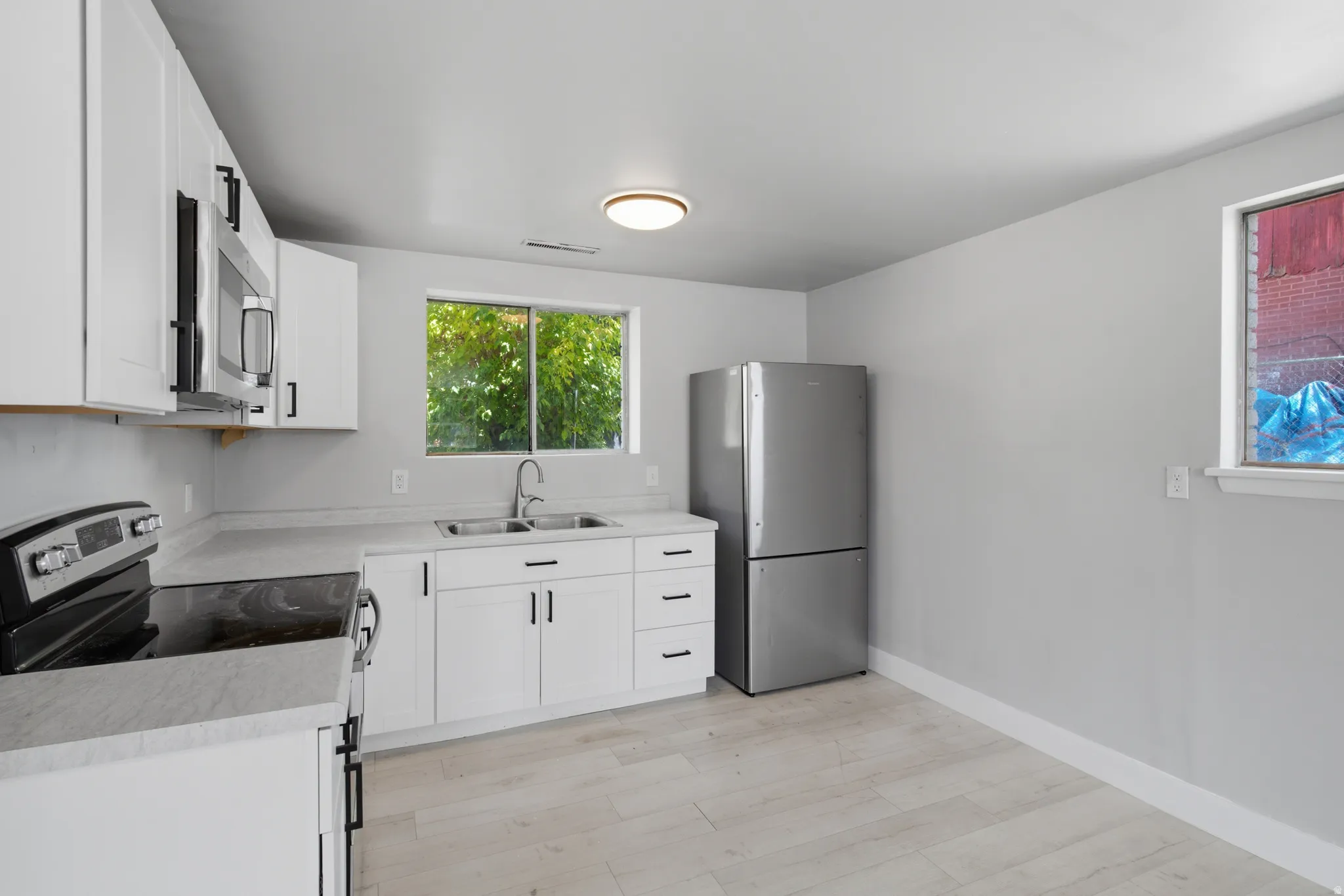 White shaker-style cabinetry with matte black hardware, stainless steel appliances, light-toned wood-finish flooring, and a double basin sink