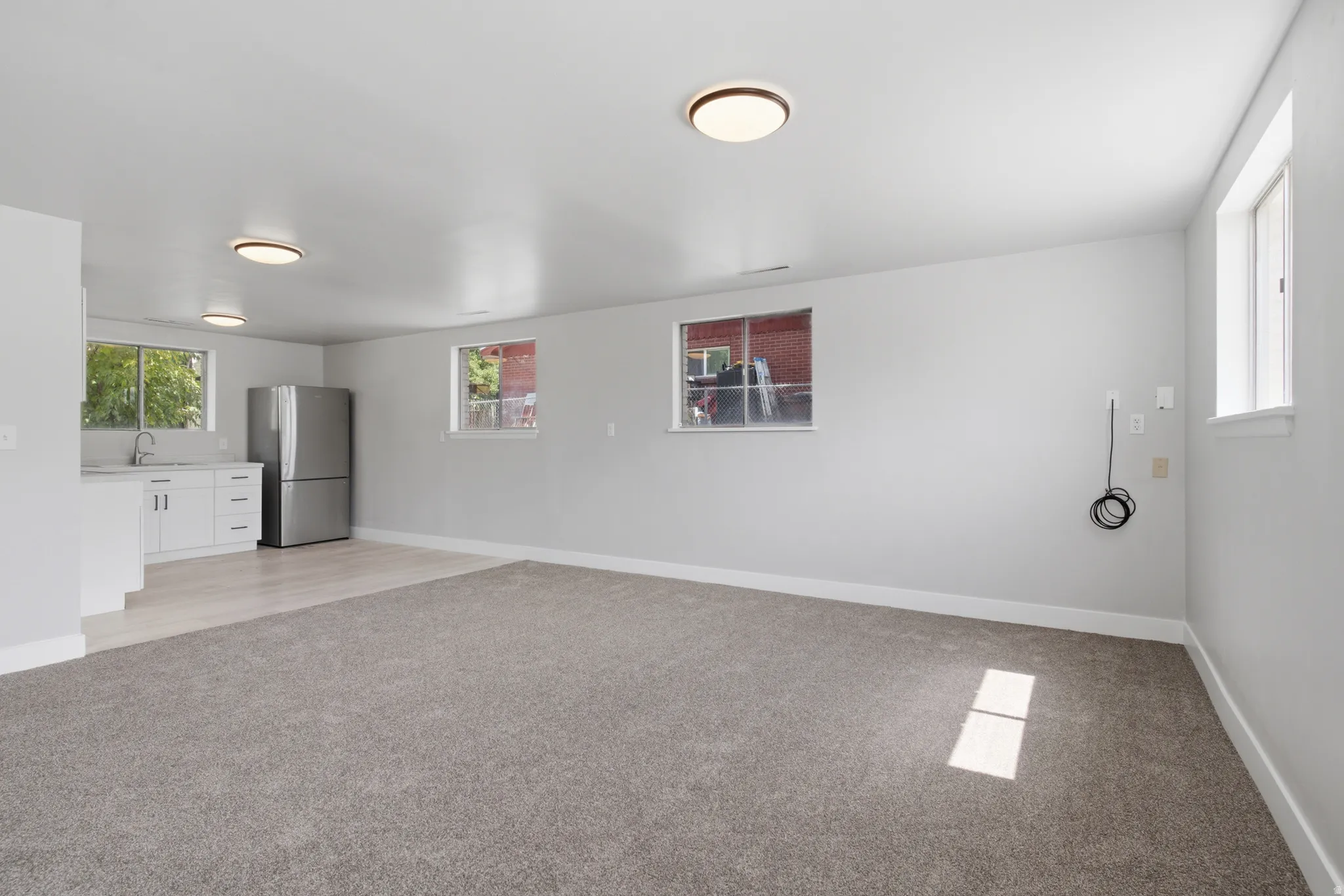Spacious room featuring new carpeting, light wood-finish flooring, white cabinetry, a stainless steel refrigerator, and multiple windows