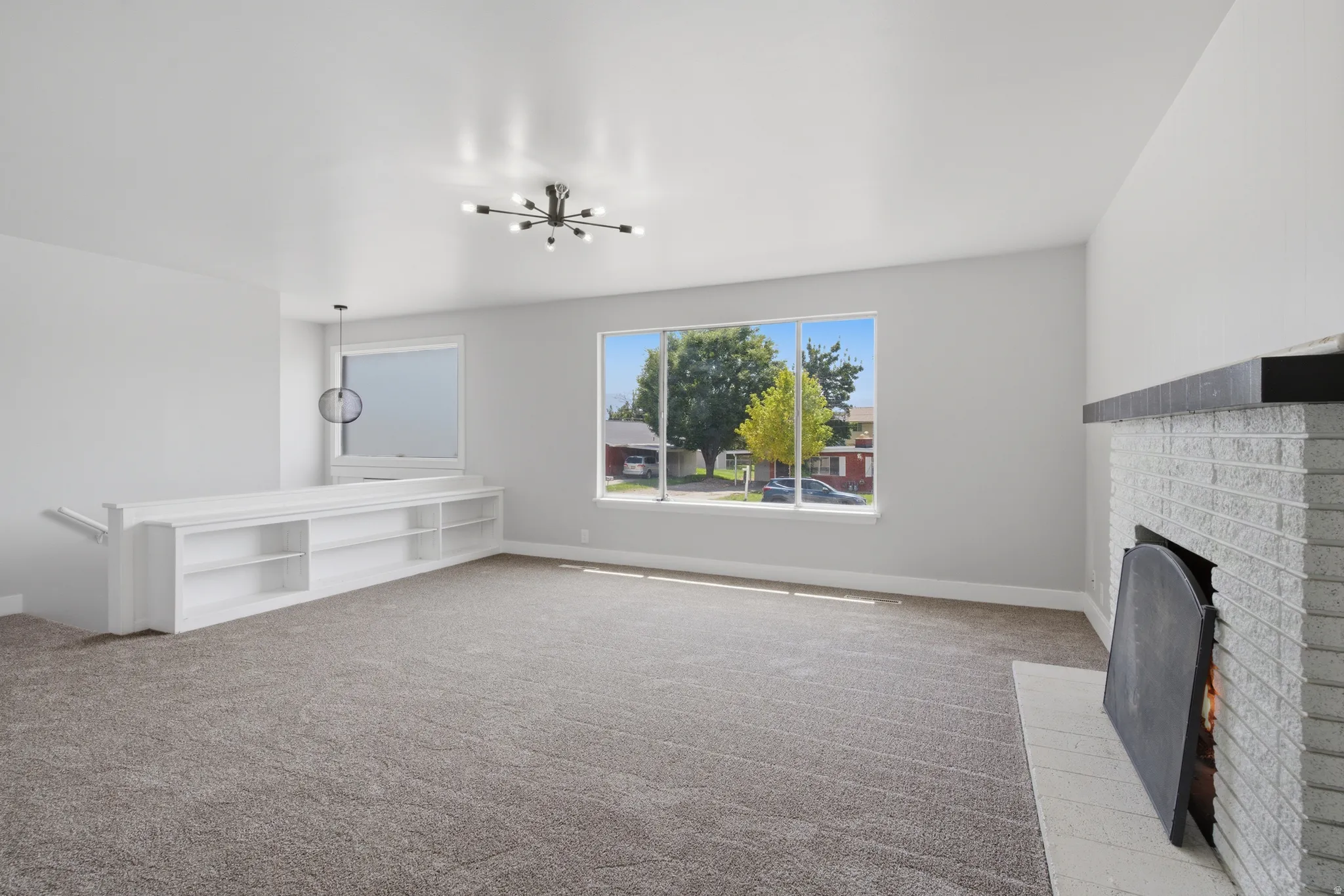 Expansive living area featuring a white brick fireplace with a dark mantel, large picture windows, and built-in shelving