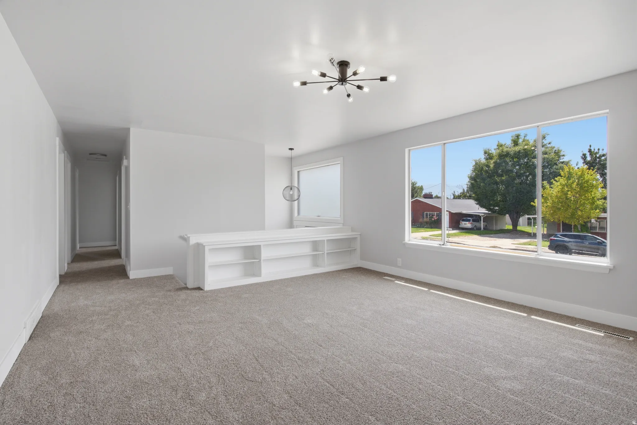 Expansive room featuring light gray carpeting, a large picture window, and a modern sputnik-style ceiling fixture