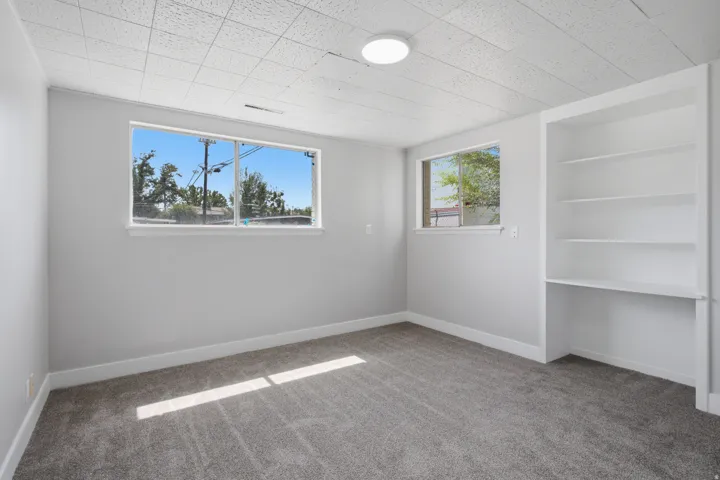 Built-in shelving, flush-mount ceiling light, two windows, and textured ceiling