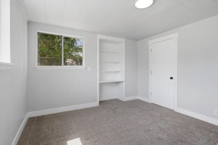 Built-in shelving with desk space, light gray walls, dark gray carpet, white trim, and a flush mount ceiling light