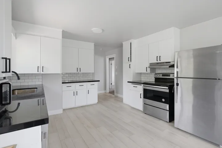 Modern kitchen featuring white cabinetry, dark countertops, a subway tile backsplash, stainless steel appliances, and light wood-finish flooring