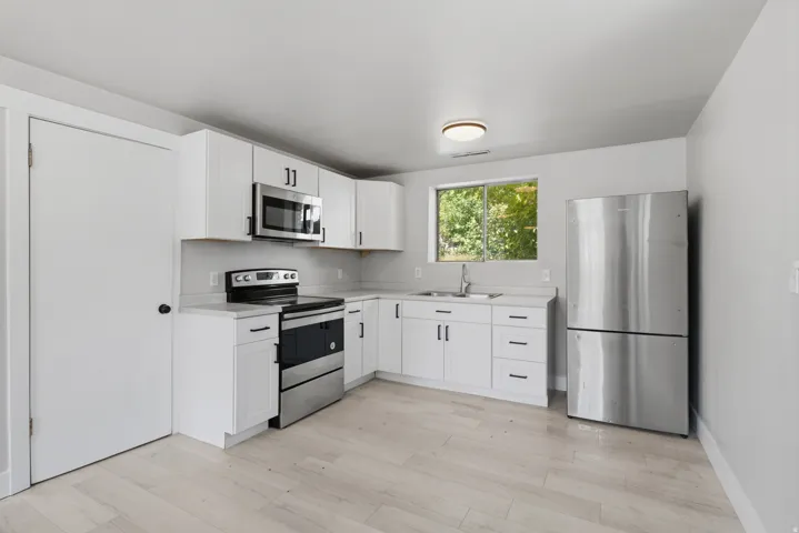 White cabinetry with matte black hardware, stainless steel appliances, light-toned flooring, and a window