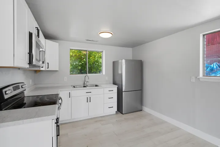White shaker-style cabinetry with matte black hardware, stainless steel appliances, light-toned wood-finish flooring, and a double basin sink