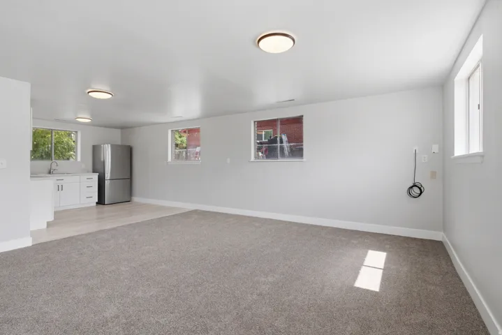 Spacious room featuring new carpeting, light wood-finish flooring, white cabinetry, a stainless steel refrigerator, and multiple windows
