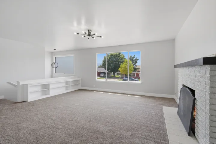 Expansive living area featuring a white brick fireplace with a dark mantel, large picture windows, and built-in shelving