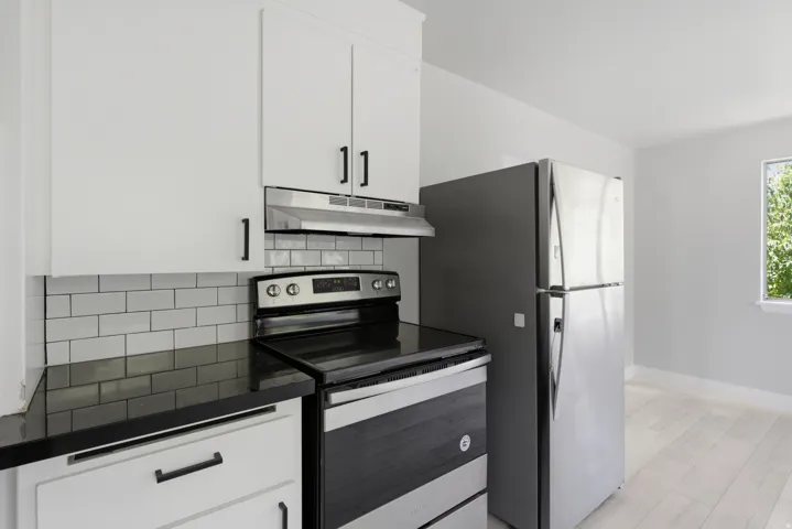 White cabinetry with matte black hardware, dark countertops, subway tile backsplash, stainless steel appliances, and light wood-finish flooring
