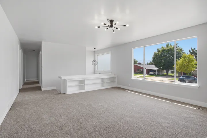 Expansive room featuring light gray carpeting, a large picture window, and a modern sputnik-style ceiling fixture