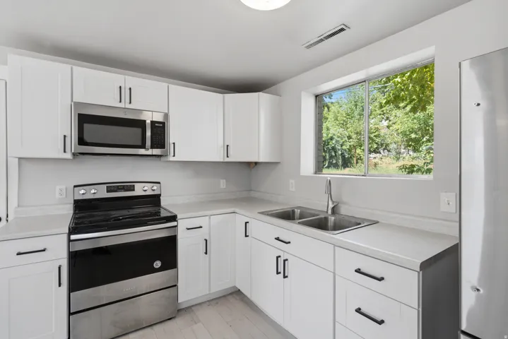 White shaker-style cabinetry with black hardware, light-toned countertops, stainless steel appliances, and a dual-basin sink with a gooseneck faucet