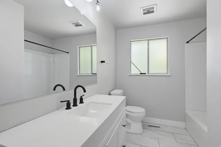 White vanity with an integrated rectangular sink, matte black faucet, and full-width mirror