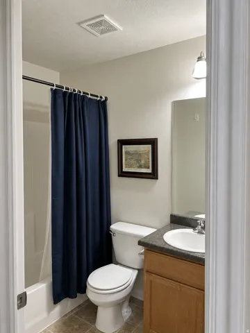 Full bathroom featuring a single vanity with wood-finish cabinetry, a toilet, a built-in tub with shower, and tile flooring