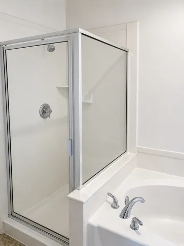 Shower enclosure with clear glass paneling, polished chrome hardware, and built-in shower shelving. Seperate soaking tub
