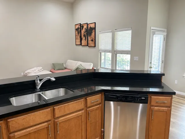 Kitchen island with black countertops, stainless steel sink, and dishwasher